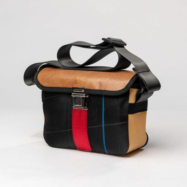 Eine Handtasche in Schwarzem Stoff mit gelben blauen und roten Streifen und einem Lederdeckel mit Schnalle und Druckknopf in Silber