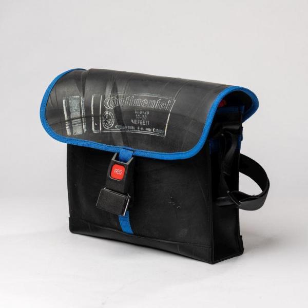 Eine Schwarze Umhängetasche aus Schlauchmaterial mit blauem Einband, einem Gurtverschluss und einem roten Knopf mit der Aufschrift Press